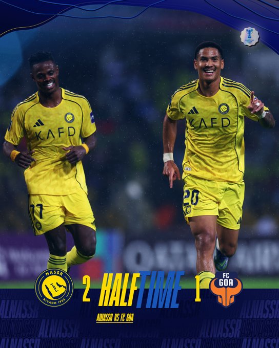 Two soccer players in yellow Al Nassr jerseys with black shorts stand on a green field during halftime, one with number 81 raising arms in celebration, the other with number 20 smiling and pointing, scoreboard graphic at bottom reads Al Nassr 2 Half Time 1 FC Goa.