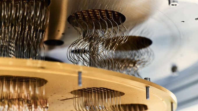 Close-up view of intricate quantum computing hardware components including multiple curved metallic connectors and wires emerging from circular ports on a metallic surface with gold accents and reflective surfaces suggesting advanced superconducting elements
