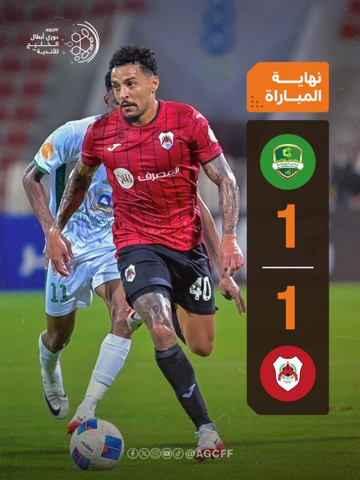 Two soccer players in action on a green field during a match, one in a red jersey with tattoos on his arms dribbling a white soccer ball while wearing black shorts and red socks, the other in a blue and white jersey approaching from behind in white shorts and socks, stadium seating and banners in the blurred background, overlaid graphics show score 1-1 with flags and emblems of Al-Nahda Omani in green and Al-Rayyan Qatari in red.