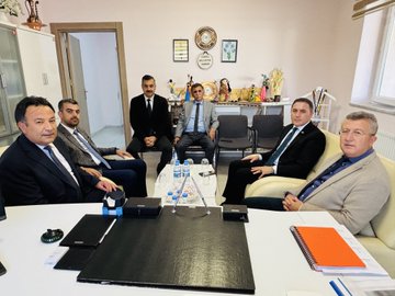 First image shows a group of about 15 professionals in suits and formal attire standing on a paved area outside a white building with green signs reading Tunceli Halk Egitimi Merkezi and Halil Rufai, under a clear sky with trees nearby. Second image depicts six men in suits seated around a black table in an indoor room with beige walls, decorative items like clocks and vases on shelves, water bottles and documents on the table. Third image features eight people including men in suits and a woman in a white top standing in a white-walled room with a clock, blue chairs, and a door. Fourth image shows ten individuals in business attire gathered in a similar indoor space with a clock, red chair, and blue sofa.