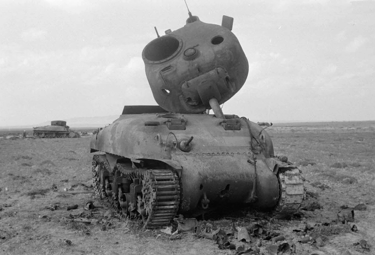 The turret hatch has also blown off and the rubber pads are burned off the starboard track.  In the background is another knocked out Sherman, it appears the turret might have blown off and landed upside down on the hull