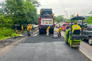 Multiple images show groups of workers in yellow uniforms and helmets performing asphalt patching on a rural road. They use shovels, rakes, and a green compactor machine to spread and level hot asphalt from red dump trucks marked with COVIAL and CAMVIO logos. Surrounding elements include lush green trees, parked vehicles like sedans and SUVs, traffic cones, and a partly cloudy sky. One image focuses on workers loading and spreading material near a truck, another on compacting the surface with a roller, and others capture the team coordinating the repair process.