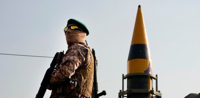 First image shows a soldier wearing camouflage uniform green beret gold-tinted goggles and face covering standing in profile holding a rifle with a yellow conical missile mounted on a launcher behind him in a desert landscape under clear sky. Second image depicts a tall black missile with yellow tip and black stripes launching vertically from a metal platform in sandy desert area with orange flames smoke billowing from base and Iranian flag visible nearby.