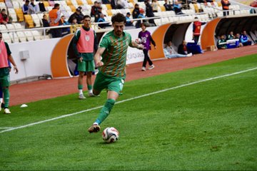 First image shows soccer players in green and white uniforms facing off on a grassy field with a ball at their feet, surrounded by a stadium crowd in orange seats and orange barriers, scoreboard overlay reads MYS 0 0 Erciyes with team logos. Second image captures a player in green striped jersey kicking a white soccer ball on green turf, other players in training gear visible in background near orange barriers and stadium seating. Third image depicts a player in green uniform dribbling a white soccer ball on the field, another player in white nearby, stadium with yellow seats and orange structures in background. Fourth image features a coach in black suit standing arms crossed on the sideline next to a player in red uniform, green field and stadium seating visible.