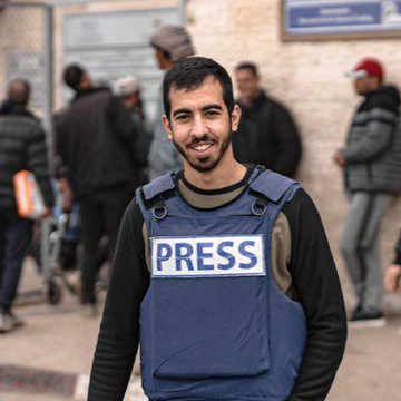 First image shows a man wearing a blue press vest labeled PRESS over dark clothing standing in an outdoor urban area with beige walls and a blue sign nearby surrounded by several people in jackets and hats some wearing red caps in a busy street setting. Second image displays a portrait of a man with a beard and short hair against a black background with Arabic text overlay reading what appears to be a name or title in white script.