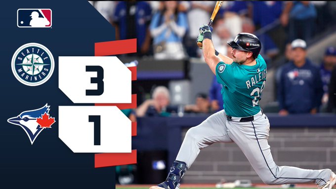 El jugador de béisbol Randy Arozarena con el uniforme verde azulado número 23 de los Marineros de Seattle balancea un bate con mango verde en un lanzamiento durante un juego contra los Azulejos de Toronto, con la multitud del estadio de fondo, la pantalla de puntuación que muestra a los Marineros 3 y los Azulejos 1, el logotipo de la MLB, los logotipos de los equipos de los Marineros y los Azulejos visibles.