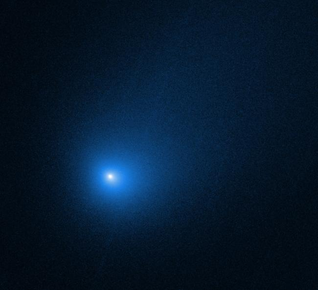 Dark cosmic background with scattered small white stars and a prominent bright blue glowing light at the center, representing the comet 3I/ATLAS in space.