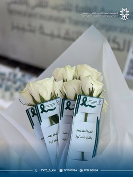 First image shows a table with multiple blue water bottles, white cups, and snacks on a white cloth in a modern room with geometric wall patterns and a stand holding a framed QR code. Second image displays a screen presenting a question about mental health in Arabic with illustrative icons and a cartoon figure, set in an indoor space with a surveillance camera and railing. Third image features a wall with the TVTC logo and Arabic-English text for Technical and Vocational Training Corporation, alongside a table of water bottles and a stand with a QR code. Fourth image depicts several bouquets of white roses wrapped in green paper with Arabic text on ribbons symbolizing awareness.