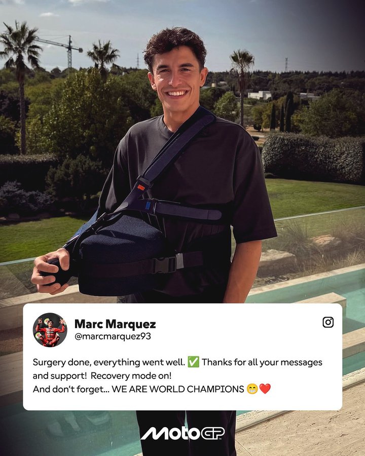 Young man with curly dark hair wearing a black t-shirt and carrying a black backpack stands smiling outdoors near a swimming pool with palm trees and buildings in the background under sunny sky. Inset shows him in red racing suit on motorcycle. Text overlay reads Surgery done everything went well Thanks for all your messages and support We are World Champions with checkmark heart emojis and MotoGP logo.