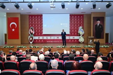 First image shows a formal auditorium with red and white decorations Turkish flags flower arrangements and a banner reading OSTİM a man in a suit stands at a podium speaking to an audience of seated attendees including some taking photos. Second image depicts a large group photo of diverse individuals in formal attire including suits traditional robes and uniforms standing in front of a red backdrop with the text 2025-2026 Akademik Yılı Açılış Töreni and the OSTİM logo. Third image features three men on stage one bald in a suit one with glasses in a suit and one in a red robe holding a blue plaque in front of a screen displaying 2025-2026 Yılı and OSTİM Teknik Üniversitesi with flower decorations and hashtag OSTİM. Fourth image shows two men in suits one holding a small model rocket on a stand in front of a brick wall with the OSTİM Teknik Üniversitesi logo and name in red letters plants visible nearby.
