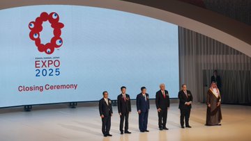 First image shows a large stage with a screen displaying Expo 2025 Closing Ceremony in English and Japanese, featuring five men in suits and one in traditional Saudi thobe standing together under curved architecture. Second image depicts four young men in khaki uniforms and hats holding and presenting a white flag with a blue circle emblem on a stage with golden poles and audience below. Third image captures two men in suits and one in Saudi thobe and red checkered headscarf shaking hands, with a boy scout in uniform standing nearby, against a backdrop of curtains and screens. Fourth image shows elderly men in suits clapping, a man in thobe holding a document, and a boy scout saluting, positioned on a wide stage with draped backgrounds.
