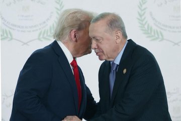 First image shows two men in dark suits standing side by side with thumbs up gestures, one wearing a red tie and American flag pin, the other a blue tie and small badge, against a white backdrop with Arabic script and laurel designs. Second image depicts the same men shaking hands formally. Third image captures them facing each other closely with serious expressions. Fourth image shows them standing together smiling slightly. The backdrop features symmetric Arabic text and olive branch motifs.
