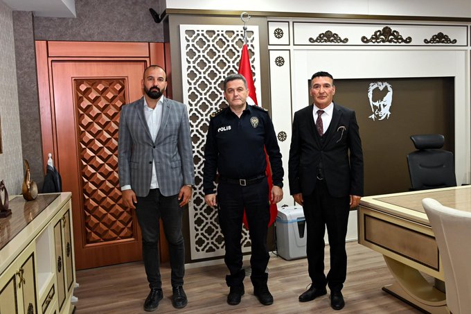 İlk görüntüde üç adam resmi bir ofiste oturuyor bir polis üniformalı adam ortada masa başında iki sivil giyimli adam yanlarda koltuklarda Türk bayrakları duvarlarda asılı dekoratif unsurlar var. İkinci görüntüde üç adam ayakta poz veriyor polis üniformalı adam ortada iki sivil giyimli adam yanlarda Türk bayrağı ve polis amblemi duvarlarda görülüyor masa ve koltuklar ofis ortamında.
