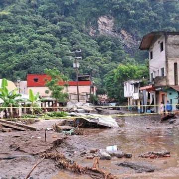 Primera imagen muestra un area residencial en una region montanosa con casas de colores como rojo y blanco rodeadas de vegetacion exuberante, pero con inundacion severa, escombros flotantes, bananos y cinta amarilla de precaucion bloqueando el paso en medio de agua fangosa y lodo. Segunda imagen es una vista aerea de un area urbana con edificios, vehiculos estacionados y cultivos inundados por agua turbia, mostrando calles y estructuras sumergidas en un paisaje montanoso. Tercera imagen presenta a varios hombres uniformados con chalecos y cascos, algunos en blanco y azul, usando palas para remover lodo y escombros en un terreno fangoso cerca de edificios y arboles caidos.