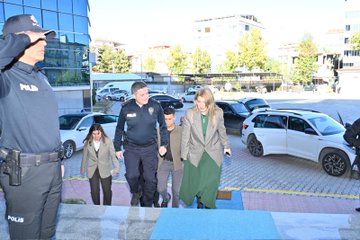 First image shows two individuals standing formally in a room adorned with Turkish flags on either side and a portrait on the wall behind them. A woman in a green dress and gray jacket stands next to a man in a navy police uniform with badges. They are positioned in front of a podium with microphones and additional flags including the Turkish and another red-white flag. The setting appears official with wooden paneling and ceiling lights. Second image depicts a group of people walking down outdoor steps near parked cars under a clear sky. Several men in suits and police uniforms escort a woman in a green dress and another in gray attire. Police officers in navy uniforms with hats and belts are visible guiding the group. Cars including white and silver vehicles are parked nearby with yellow barriers. Third image features five people standing on steps in front of a building entrance marked with Malatya İl Emniyet Müdürlüğü sign and emblems. A woman in blue jacket white shirt and jeans stands beside a man in police uniform then a woman in green dress gray jacket followed by two men in gray suits. The building has glass doors columns and red accents with Turkish flags.