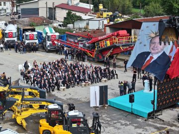 First image shows a group of officials in suits cutting a red ribbon on a blue stage with Turkish flags and large banners of President Recep Tayyip Erdogan, under a metal frame structure. Second image depicts officials standing beside red Boratas branded construction machinery including a crusher and excavator in an industrial yard. Third image captures officials seated on chairs near yellow and red heavy machinery like a loader and crusher, with some wearing work vests. Fourth image features a large banner of President Recep Tayyip Erdogan and groups of officials near yellow Komatsu excavators, red fire trucks, and other construction equipment in an open yard with buildings in the background.