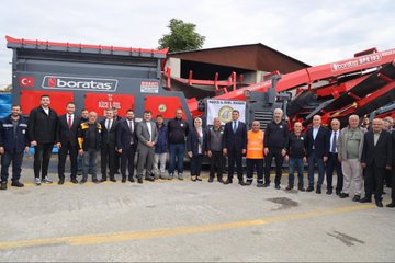 First image shows a group of officials in suits cutting a red ribbon on a blue stage with Turkish flags and large banners of President Recep Tayyip Erdogan, under a metal frame structure. Second image depicts officials standing beside red Boratas branded construction machinery including a crusher and excavator in an industrial yard. Third image captures officials seated on chairs near yellow and red heavy machinery like a loader and crusher, with some wearing work vests. Fourth image features a large banner of President Recep Tayyip Erdogan and groups of officials near yellow Komatsu excavators, red fire trucks, and other construction equipment in an open yard with buildings in the background.