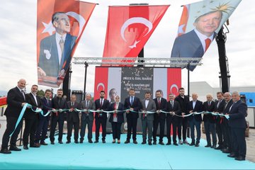 First image shows a group of officials in suits cutting a red ribbon on a blue stage with Turkish flags and large banners of President Recep Tayyip Erdogan, under a metal frame structure. Second image depicts officials standing beside red Boratas branded construction machinery including a crusher and excavator in an industrial yard. Third image captures officials seated on chairs near yellow and red heavy machinery like a loader and crusher, with some wearing work vests. Fourth image features a large banner of President Recep Tayyip Erdogan and groups of officials near yellow Komatsu excavators, red fire trucks, and other construction equipment in an open yard with buildings in the background.