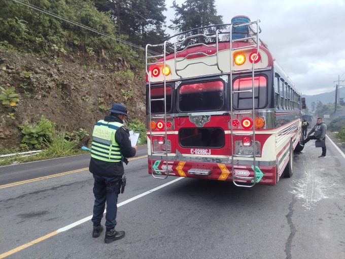 Primera imagen muestra la parte trasera de un autobus escolar amarillo y rojo con luces rojas encendidas estacionado en una carretera empinada y curvada en un area montanosa con vegetacion verde y niebla, un oficial de transito con chaleco verde reflectante, sombrero azul y pantalon negro sosteniendo un portapapeles esta parado junto al vehiculo inspeccionandolo, el autobus tiene la placa D-08601 y marcas de seguridad como triangulo reflectante, segunda imagen muestra la parte trasera de un autobus amarillo con puertas abiertas y pasajeros dentro, un oficial de transito con chaleco verde reflectante, sombrero azul y pantalon negro sosteniendo un portapapeles esta parado junto a la puerta abierta inspeccionando, hay bolsas y equipaje cerca de la puerta, el autobus tiene la placa MDR y esta en una carretera con vegetacion y montanas de fondo bajo cielo nublado.
