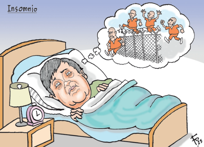 Cartoon illustration shows a man with dark hair and a round face lying in bed under blue covers, eyes closed but with a worried expression, head on a white pillow next to a pink alarm clock and a lit lamp on a wooden nightstand. Above him, a thought bubble displays several elderly men in orange prison jumpsuits running and waving behind a chain-link fence enclosure. The title Insomnio appears at the top left, and the artists signature Fo is at the bottom right.