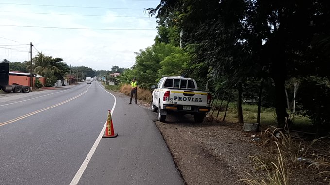 First image shows a white Provial truck parked on the roadside of a highway with trees and vegetation nearby a person in high-visibility gear stands near orange traffic cones next to the vehicle. Second image depicts an overturned large truck with multiple wheels visible on its side lying on a curved road surrounded by greenery and trees another vehicle is in the background with orange cones placed around the scene for safety.