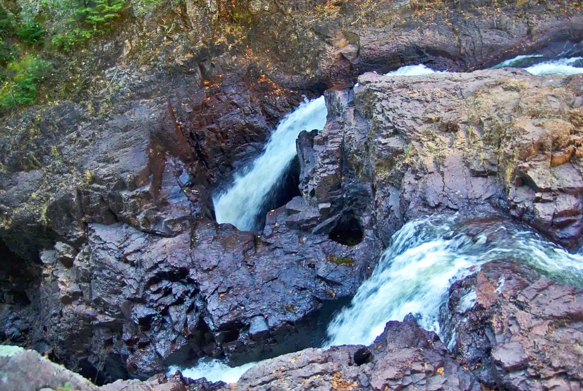 geologyBits's tweet photo. 🟥 ⛏️ The Devil’s Kettle
a mesmerizing geological oddity in Minnesota’s Judge C.R. Magney State Park along the Brule River, features a dramatic bifurcation where the river splits over a resistant rhyolite outcrop.
❤️ 🔁 #DevilsKettle #RhyolitePothole
🎞️ @KayakAnglingMinnesota
▶️ A hard, felsic volcanic rock akin to granite with embedded quartz and feldspar crystals, creating two 25-foot waterfalls: one cascading into a serene pool.
The other plunging into a cavernous, 20-foot-wide pothole that mysteriously swallows the flow, only to reemerge about 200 yards downstream amid boulders.
Confirmed by streamflow measurements showing near-equal volumes above and below the falls.
This feature formed during the Proterozoic era around 1.1 billion years ago as part of the North Shore Volcanic Group’s massive rhyolitic eruptions tied to the Midcontinent Rift.
When silica-rich magma extruded as thick flows that cooled rapidly into jointed sheets.
Over subsequent eons, Pleistocene glaciation scoured the landscape, and post-glacial fluvial erosion by the Brule River exploited vertical joints in the rhyolite.
With the pothole specifically excavated through abrasive potholing, swirling pebbles and grit in turbulent eddies grinding a deep, cylindrical cavity that connected to a subsurface channel.