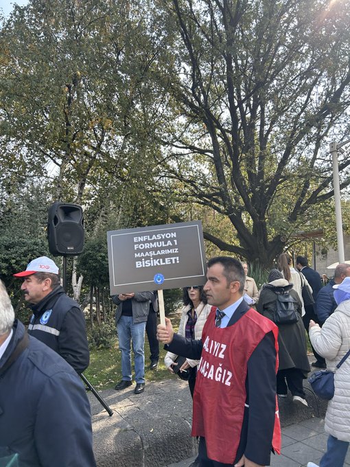 First image shows a man in a cap and jacket holding a black sign reading 3600 EK Gosterge Istiyoruz near a government building with Turkish flag, surrounded by other people and vehicles on a sunny day. Second image depicts several men in suits holding blue and red signs with messages like MEMUR EMEKLI ARTISI YOK SAĞLIK EMEĞİ and ÖĞRETIM EMEĞİ, standing in an open area with trees and flags. Third image features a man in a blue jacket holding a white sign reading EK ZAM VE REFAH PAYI ISTIYORUZ near trees and a speaker setup in a grassy area. Fourth image shows a group including a man in a red vest holding a sign reading ENFLASYONA KARŞI BİRLİK OL and another with MEMUR EMEKLİSİ, near trees and a speaker on grass.