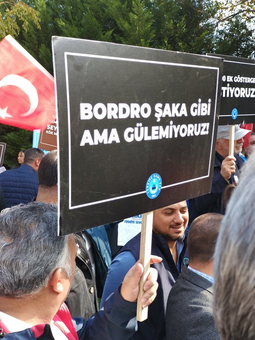 First image shows a large group of men in suits and ties gathered outdoors near trees, holding red banners with white text reading MAASLARDA REFORM YAP and ADALET, surrounded by microphones and cameras from media, with Turkish flags and union banners in the background. Second image displays two brown posters side by side, one marked 2008 with text ZAM VE REFAH PAYI ÖNCESI VE SONRASI AYIRIMI KALDIRILSIN, the other with similar content, held by individuals near blue Türk Sağlık-Sen flags and a Turkish flag. Third image features a black-framed white sign held by a man, reading 8 EK GÖSTERGE BORÇDURO ŞAKA GİBİ AMA GÜLEMIYORUZ, with a blue union logo, next to a red Turkish flag and other protesters. Fourth image depicts people in blue vests and suits holding brown banners stating CON MAZANANDAN AZ KAZANANDAN ÇOK VERGİ AL VERCH, with Turkish flags and additional protest signs in a green outdoor setting.