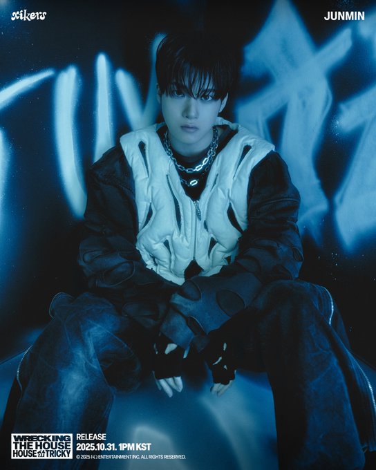 First image depicts JUNMIN seated in a dimly lit blue environment wearing a white structured vest over black shirt and pants accessorized with layered necklaces and black gloves hands resting on knees. Text overlays include xikers logo album title HOUSE OF TRICKY WRECKING THE HOUSE release date 2025.10.31 1PM KST and member name JUNMIN. Second image is a close-up portrait of JUNMIN facing forward with wet-look black hair blue lighting on face wearing white vest black shirt and necklaces. Text overlays match the first image with xikers branding and release information.