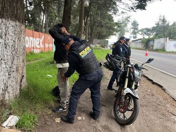 First image shows multiple uniformed police officers in yellow vests marked POLICIA NACIONAL CIVIL standing along a roadside near trees and a green building with a sign, some wearing helmets, one holding a clipboard and interacting with a man in casual clothes next to a black motorcycle, yellow tape visible on the ground. Second image depicts officers in black tactical vests and blue uniforms examining a person in white shirt and jeans beside a black motorcycle on a road flanked by trees and a red wall with COMEX text, traffic cones present. Third image features a blue police pickup truck with CHI-176 license plate and CHIMALTENANGO markings parked on a dirt shoulder near a concrete wall and trees, officers in vests walking alongside with motorcycles and cones nearby.