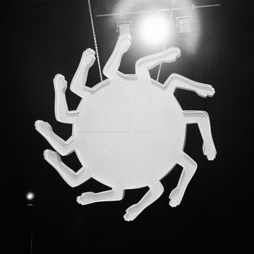 First image displays a black-and-white artistic installation on a dark stage with overhead lights, featuring a central white circular structure from which multiple arm-like appendages with hands extend outward in a radial pattern, suspended by chains. Second image shows a white album cover back with handwritten-style tracklist including song titles such as Dirty Dog at 4:22, Blow the Spot Up at 3:43, Love the Things U Hate at 4:55, and credits for vocals bass and production by JMSN and others, noting all songs written produced and arranged by Christian Berish. Third image depicts a bald shirtless man with tattoos in white pants lying posed on the floor surrounded by the same radial arm structures, with a drum set visible nearby and cables strewn about in a studio setting. Fourth image presents the album front cover with the title its only about u if you think it is, track durations listed, and a small photo of the artist performing on stage with band members and the limb sculpture in background, produced by Mixed & Mastered in LA.