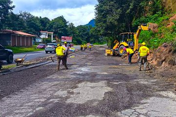 First image shows a yellow SANY wheel loader spreading asphalt on a road in a green mountainous area with workers in yellow vests nearby, excavators, and traffic cones. Second image depicts workers in yellow vests using brooms and tools near a COVIAL sign and orange cones beside a parked car on a wet road with a truck in the background. Third image features workers in yellow vests operating excavators and spreading asphalt on a road adjacent to a building and green hillside with a pickup truck present. Fourth image illustrates workers in yellow vests and helmets around a yellow asphalt paver laying material on a road with shovels, barrels, and a green hillside setting.