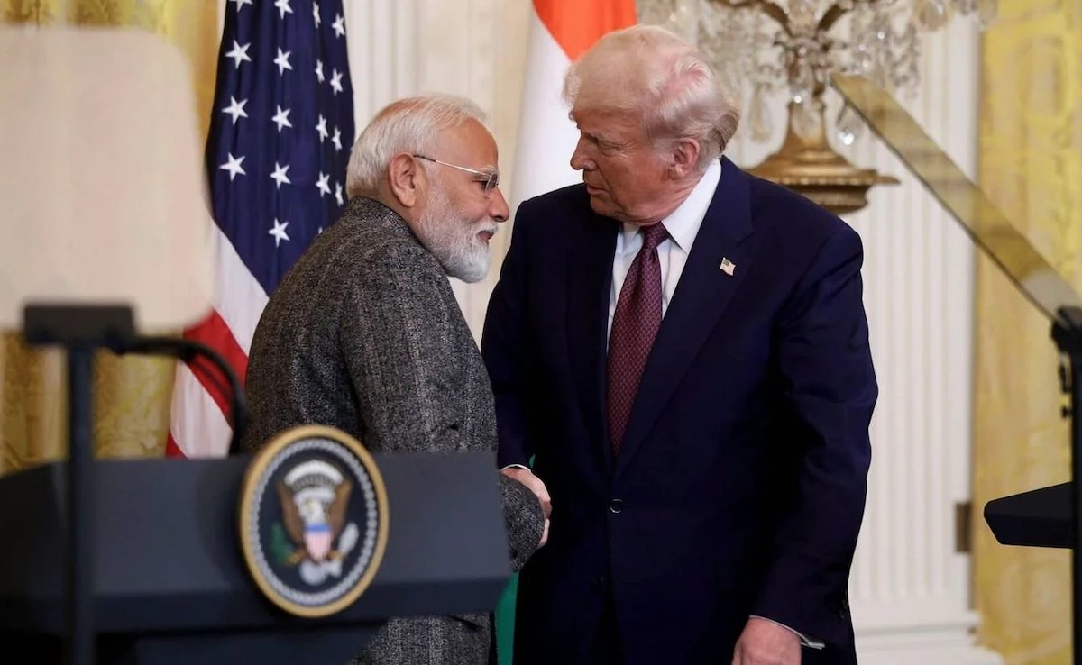 身穿灰色西装、戴着眼镜的纳伦德拉·莫迪（Narendra Modi）面对着身穿蓝色西装、打着红色领带的唐纳德·特朗普，两人都在交谈。左边是美国国旗，右边是印度国旗，前面是讲台上的总统印章，正式房间背景是华丽的枝形吊灯和金色装饰。