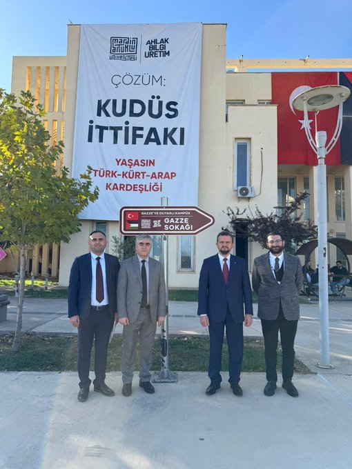 First image shows a woman in white hijab and abaya standing next to a man in dark pinstripe suit, both facing a beige stone wall with black text Gazze Sokağı engraved on a plaque, surrounded by yellow-leaved trees and parked cars on a sunny day. Second image depicts four men in suits, including one in gray and three in dark suits with ties, standing together in front of a beige stone pedestal holding an abstract white sculpted form resembling intertwined shapes or a heart, with Gazze Soykırım Anıtı text on the base, yellow trees and blue sky in background. Third image features four men in suits with ties posing outdoors near a beige building with a large white banner reading Cozum Kudüs Yaşam İttifakı and directional arrow sign for Türkiye Yasin Arat Kardeşliği and Gazze Sokak, under a lamppost and tree.