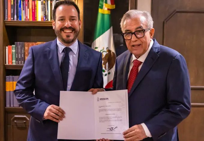 First image shows two men in dark suits standing in a library-like room with bookshelves, one younger with short hair smiling and holding left side of a white document, older with glasses smiling and holding right side, small Mexican flag on table nearby. Second image is a formal missing person report form from Durango government with header including logos, details on disappearance date October 6 2025 in Zona Dorada, physical description 1.70m tall slim build oval face brown eyes black hair, clothing black jeans and black shirt with white letters, photo of young man with glasses and cap smiling, notes on possible crime victim.