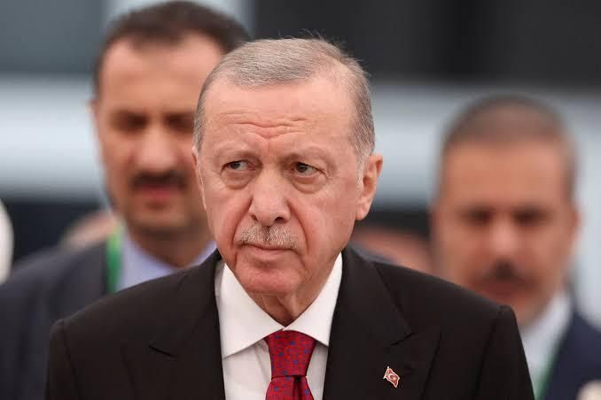 First image shows a man with short gray hair mustache and serious expression wearing a dark suit white shirt and red tie standing among other suited men in a formal setting with a Turkish flag pin on his lapel. Second image depicts a man with white hair and focused gaze in a dark suit white shirt and blue tie positioned in front of an Israeli flag in an official environment.