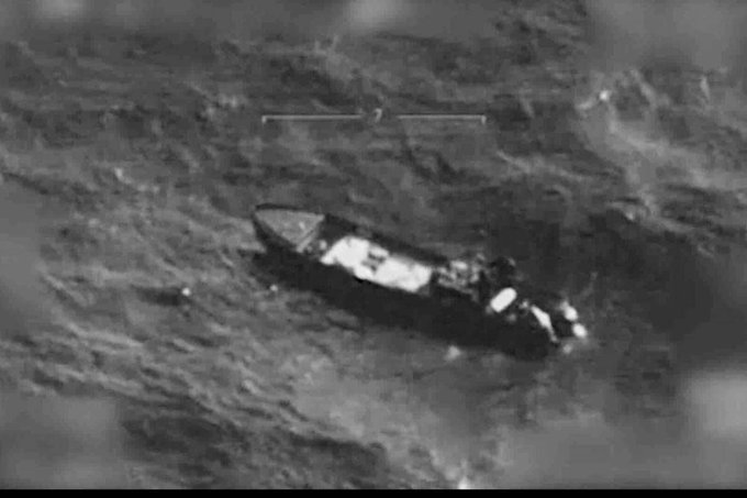 Aerial view of a partially submerged white boat with visible damage on its deck and hull floating in calm ocean waters under clear skies with a horizontal measurement scale overlaid indicating distance