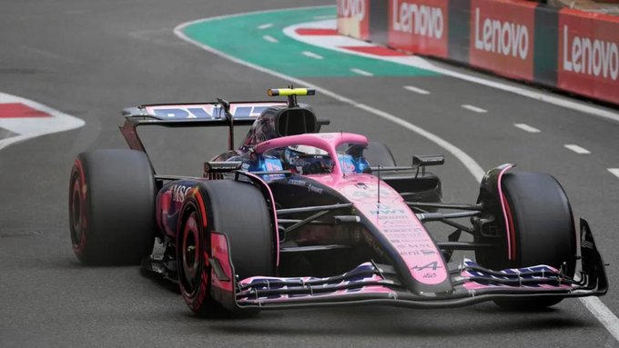 Pink Formula 1 car with black accents and Lenovo branding races on a curved asphalt track lined with green barriers and white curbing during a practice session at the United States Grand Prix circuit featuring sponsor logos on the barriers and tires visible on the car.