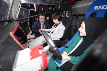 First image shows a large group of formally dressed men and women standing on a blue-lit stage holding awards during a ceremony with a banner reading Imam Hatip Basari Ornekleri Sergisi ve Odul Toreni and screens displaying participants. Second image captures several people including young individuals posing outdoors with a large red rocket model labeled ROCKET, a white drone, and flags in a courtyard setting. Third image features women in headscarves and men around a white vintage car decorated with intricate patterns and a plaque for Kizilay Imam Hatip Ortaokulu Din Geneli 1875 on a patterned floor. Fourth image depicts a man in suit interacting with two children one boy and one girl in headscarf seated in a blue racing simulator cockpit inside a metallic enclosure with screens and sponsor logos like Spar.