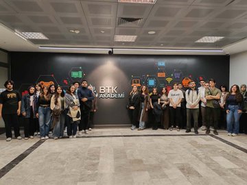 First image shows a female instructor in dark clothing standing and presenting near a whiteboard in a modern classroom with blue and white decor, geometric wall patterns, and bright overhead lights; a group of young students in casual attire sit at white desks with laptops, attentively facing forward. Second image depicts the same instructor on a large screen via video call in a similar classroom setup with blue accents, students seated at desks engaging with the presentation. Third image features a diverse group of young adults, men and women in casual clothes including jeans and t-shirts, posing together in front of a wall with the BTK Akademi logo and digital icons like circuits and networks.