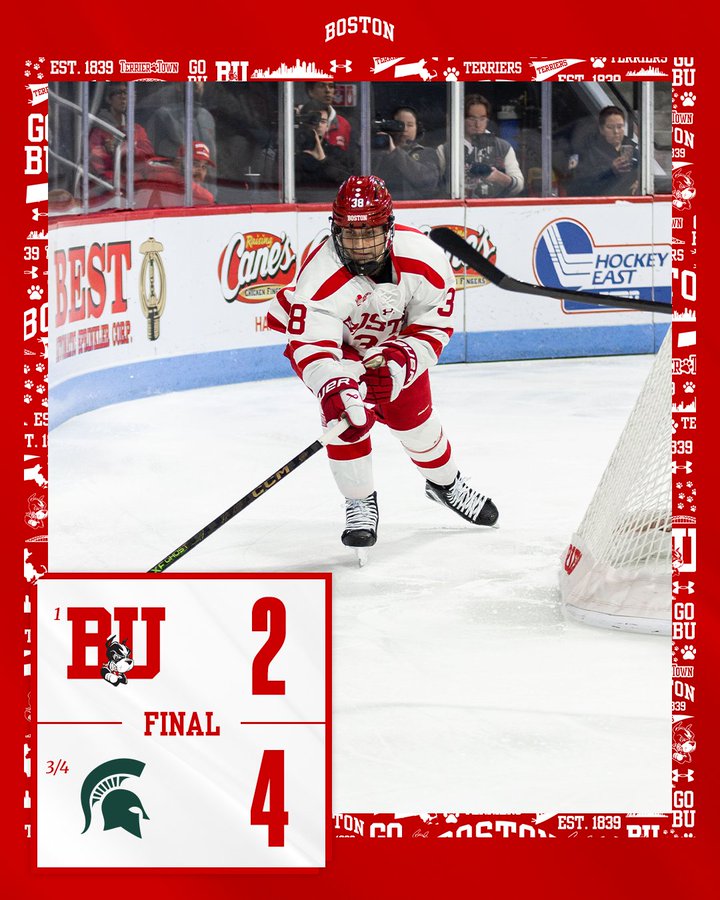 Hockey player in scarlet and white Boston University uniform with helmet skates on ice surface gripping stick positioned near net during match against green and white Michigan State Spartans team banners for Best of Boston and Canes Hockey East visible behind glass along with crowd spectators scoreboard displays final score BU 2 MSU 4