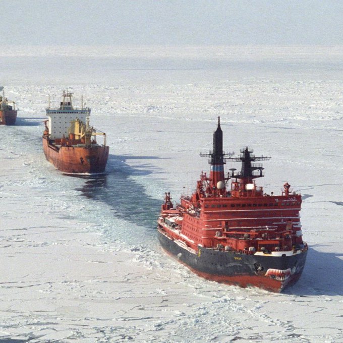 First image shows Chinese President Xi Jinping standing formally in a dark suit with a light blue shirt and blue tie smiling slightly with eyes open against a backdrop of two large red Chinese national flags with yellow stars in an indoor setting. Second image depicts a convoy of several large cargo ships including orange orange-hulled vessels with white superstructures and a prominent red-hulled Russian icebreaker ship with black funnels and antennas leading the way breaking through thick white ice-covered Arctic waters under a pale sky.