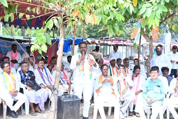 First image displays group of men and boys near school building with Telugu signage on wall surrounded by trees some wearing white shirts and orange scarves others in school uniforms with backpacks standing beside scooter. Second image captures crowd of men in white kurtas and scarves raising arms in gesture near roadside shops and parked scooters with police in uniform present. Third image shows man in white attire with orange scarf speaking into microphone at outdoor event under large tree with seated audience in chairs many wearing similar scarves and traditional clothing.