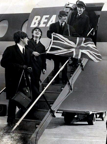 The #Beatles return from Paris on BEA flight, landing at London Heathrow Airport, holding the Union Jack flag, 5th February 1964.