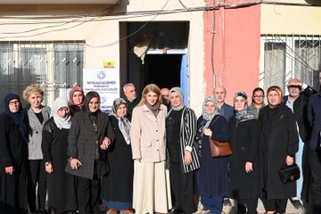 First image shows a large group of people mostly women in headscarves and modest clothing standing outside a building with a sign reading Battalgazi Belediyesi possibly indicating municipal services gathered for a formal meeting. Second image depicts a man in green jacket conversing with a blonde woman in beige coat and pants near parked cars and a building entrance with several others including women in headscarves observing. Third image captures an indoor meeting room with diverse group of men and women some in headscarves seated around a table with tea cups documents and a Turkish flag on the wall under a chandelier. Fourth image similar to first shows another group pose outside the same building with people in formal attire including coats and headscarves in front of a blue door and yellow sign.