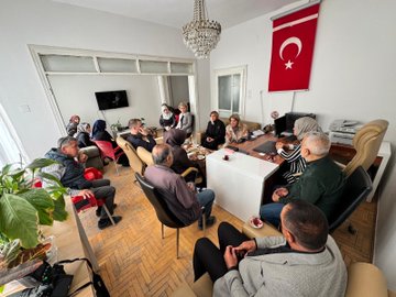 First image shows a large group of people mostly women in headscarves and modest clothing standing outside a building with a sign reading Battalgazi Belediyesi possibly indicating municipal services gathered for a formal meeting. Second image depicts a man in green jacket conversing with a blonde woman in beige coat and pants near parked cars and a building entrance with several others including women in headscarves observing. Third image captures an indoor meeting room with diverse group of men and women some in headscarves seated around a table with tea cups documents and a Turkish flag on the wall under a chandelier. Fourth image similar to first shows another group pose outside the same building with people in formal attire including coats and headscarves in front of a blue door and yellow sign.
