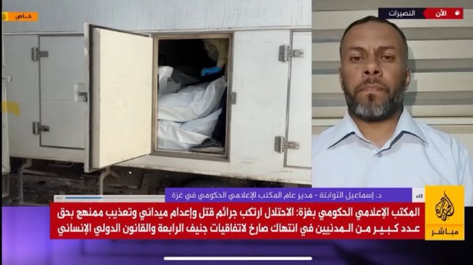 Open door of white truck reveals covered body wrapped in blue cloth lying inside on Gaza street, Arabic text overlays on screen, news anchor in light blue shirt with serious expression in split-screen view discussing incident.