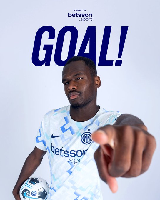 A young Black male soccer player with short hair and serious expression wears a white Inter Milan jersey with blue accents and Nike logo holding a white soccer ball under his arm while pointing forward with his right hand against a plain white background bold blue text GOAL above him and Betsson sponsor logo at bottom