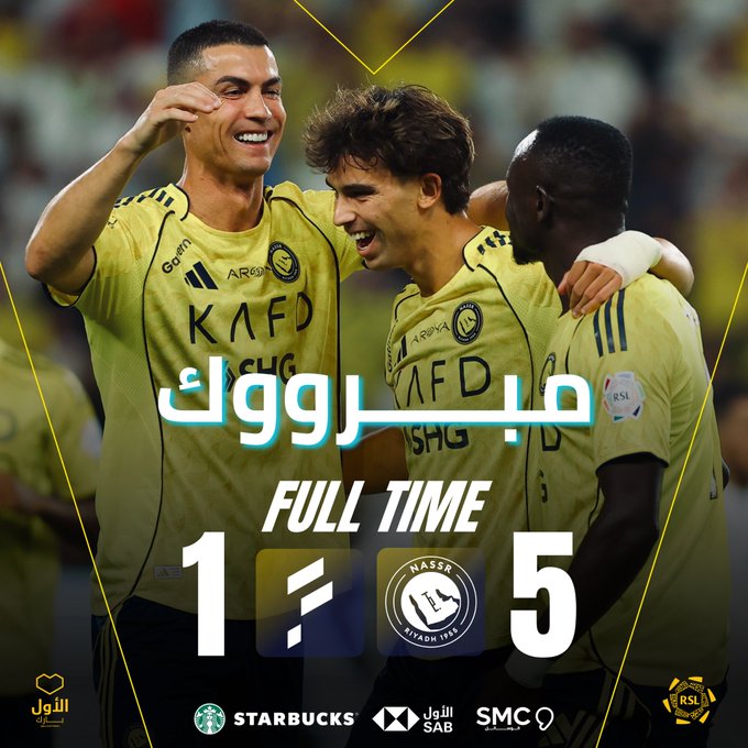 Three male soccer players in yellow Al-Fateh jerseys stand on a green field embracing and smiling, one with short dark hair touching his face, another with curly brown hair grinning, and a third with dark skin laughing, stadium seating in background, Arabic text overlay reads full time score 1-5 for Al-Nassr vs Al-Fateh, sponsor logos including Starbucks and HSBC at bottom.