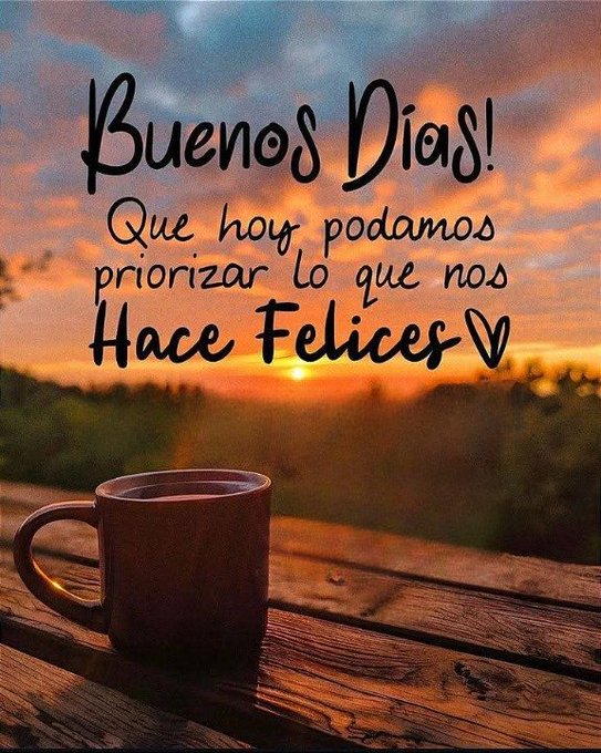 A serene outdoor scene at sunset or sunrise with orange and blue skies over green hills and a body of water in the background. A brown ceramic mug sits on a wooden table in the foreground. Bold black Spanish text overlays the image reading Buenos dias with an exclamation and a heart symbol followed by Que hoy podamos priorizar lo que nos hace felices with some repeated letters.